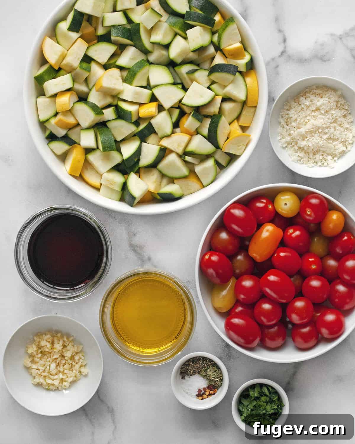 Balsamic Roasted Zucchini and Tomatoes 3 Fresh ingredients laid out on a cutting board, including vibrant green zucchini, yellow squash, ripe cherry tomatoes, a bulb of garlic, a bottle of balsamic vinegar, olive oil, and a small bowl of Parmesan cheese and herbs.