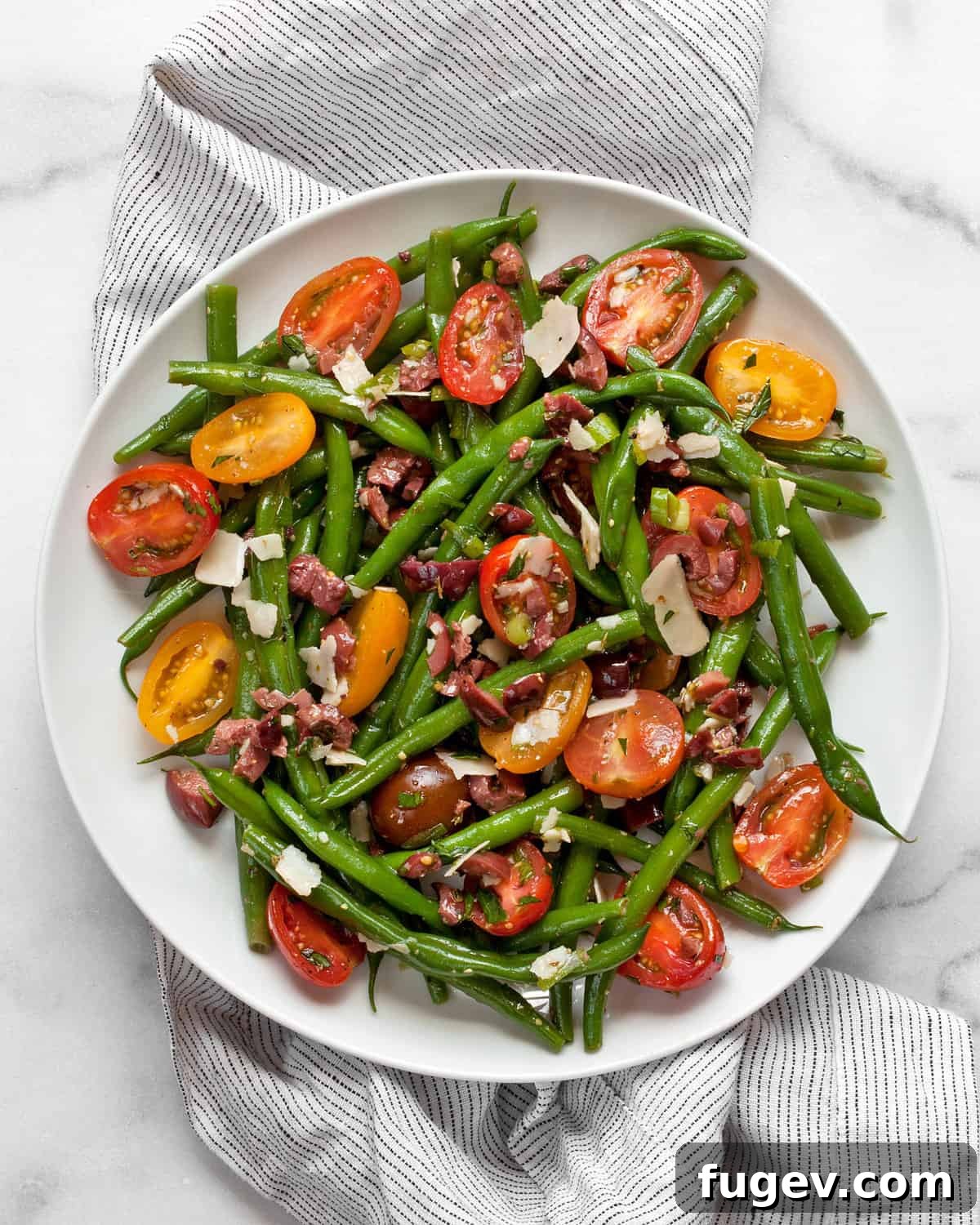 Sun-Kissed Green Bean and Olive Salad 2 Vibrant green bean, tomato, and olive salad on a white plate, garnished with fresh herbs.