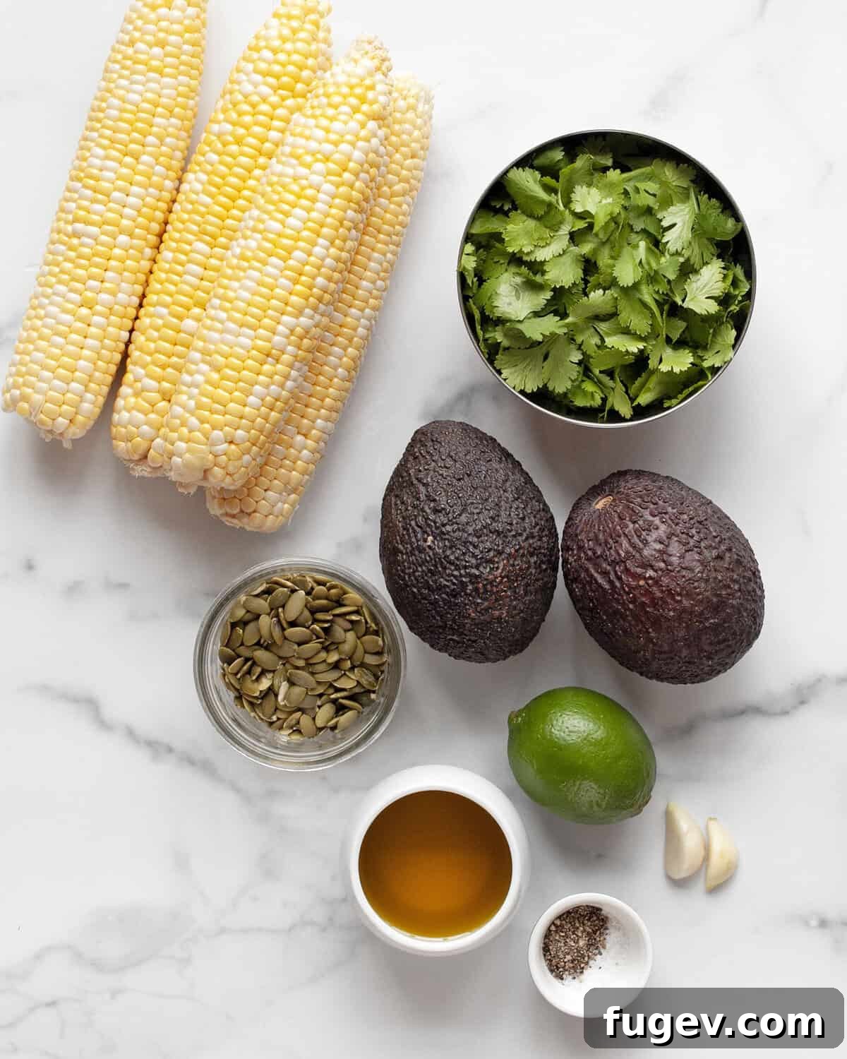 Smoky Grilled Corn with Avocado & Fresh Cilantro Pesto 3 Ingredients including corn on the cob, avocados, fresh cilantro, pumpkin seeds, garlic cloves, limes, olive oil, salt & pepper laid out on a surface.