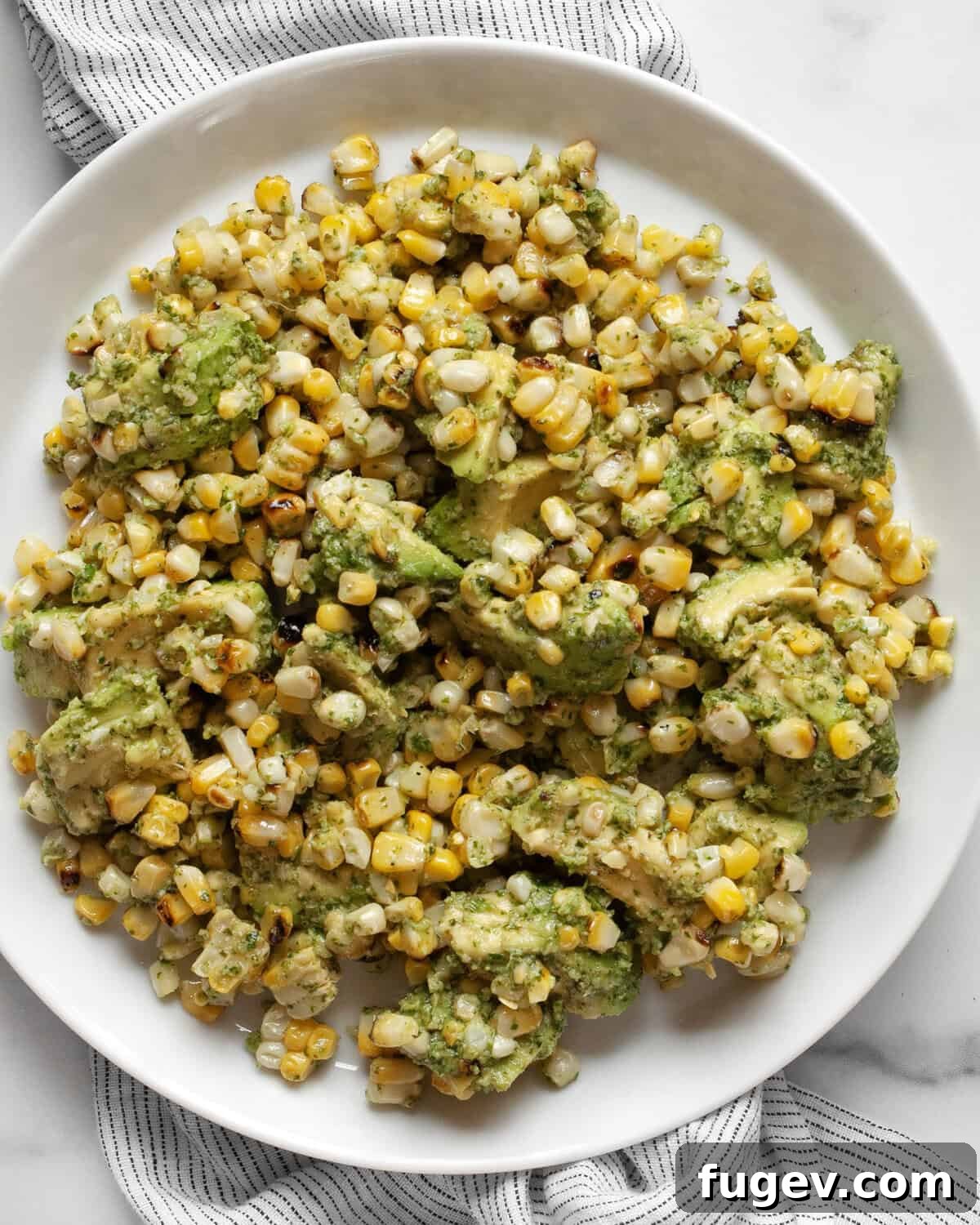 Smoky Grilled Corn with Avocado & Fresh Cilantro Pesto 6 Grilled corn and avocados with cilantro pesto served on a white plate with a fork.