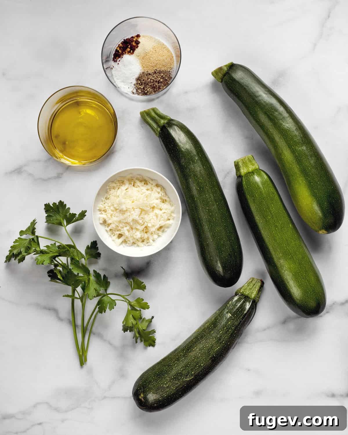 Golden Parmesan Zucchini 3 Fresh zucchini, a selection of dried spices, grated Parmesan cheese, olive oil, and fresh parsley laid out as ingredients for a recipe.