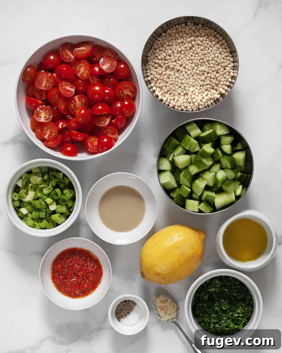 Spicy Harissa Roasted Tomato Couscous 3 A flat lay of fresh ingredients for Harissa Roasted Tomato Couscous, including cherry tomatoes, cucumbers, pearl couscous, fresh herbs, lemon, tahini, and harissa paste.