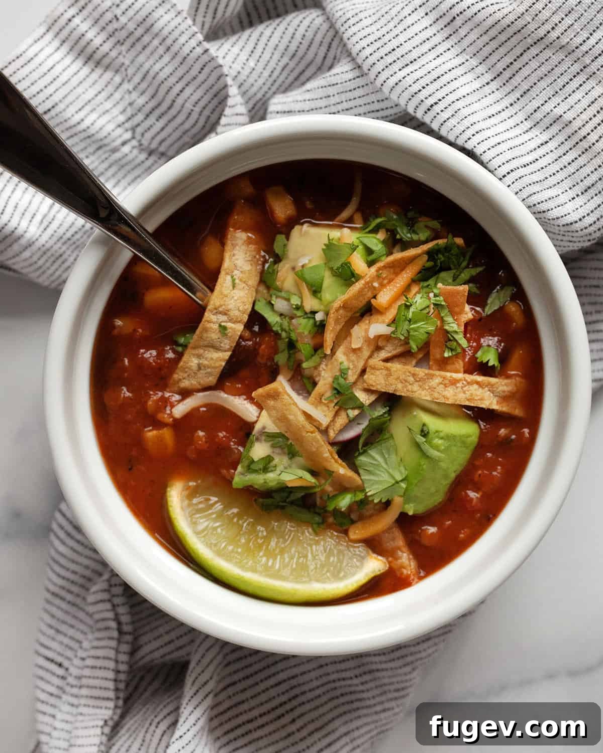 Plant-Based Slow Cooker Tortilla Soup 2 A vibrant bowl of vegetarian tortilla soup generously topped with fresh avocados, crispy baked tortilla strips, crumbled cheese, thinly sliced radishes, and bright green cilantro.