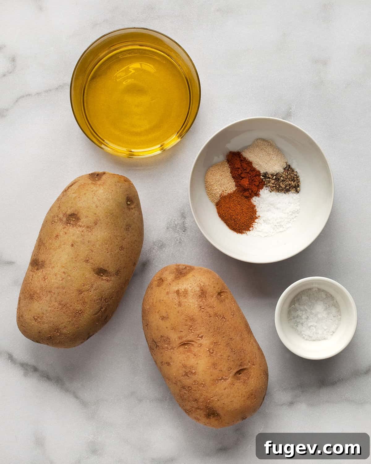 Guilt-Free Potato Crisps 3 A collection of essential ingredients laid out on a surface, including whole potatoes, a bowl of various dried spices, olive oil, and a small pile of flaky sea salt.