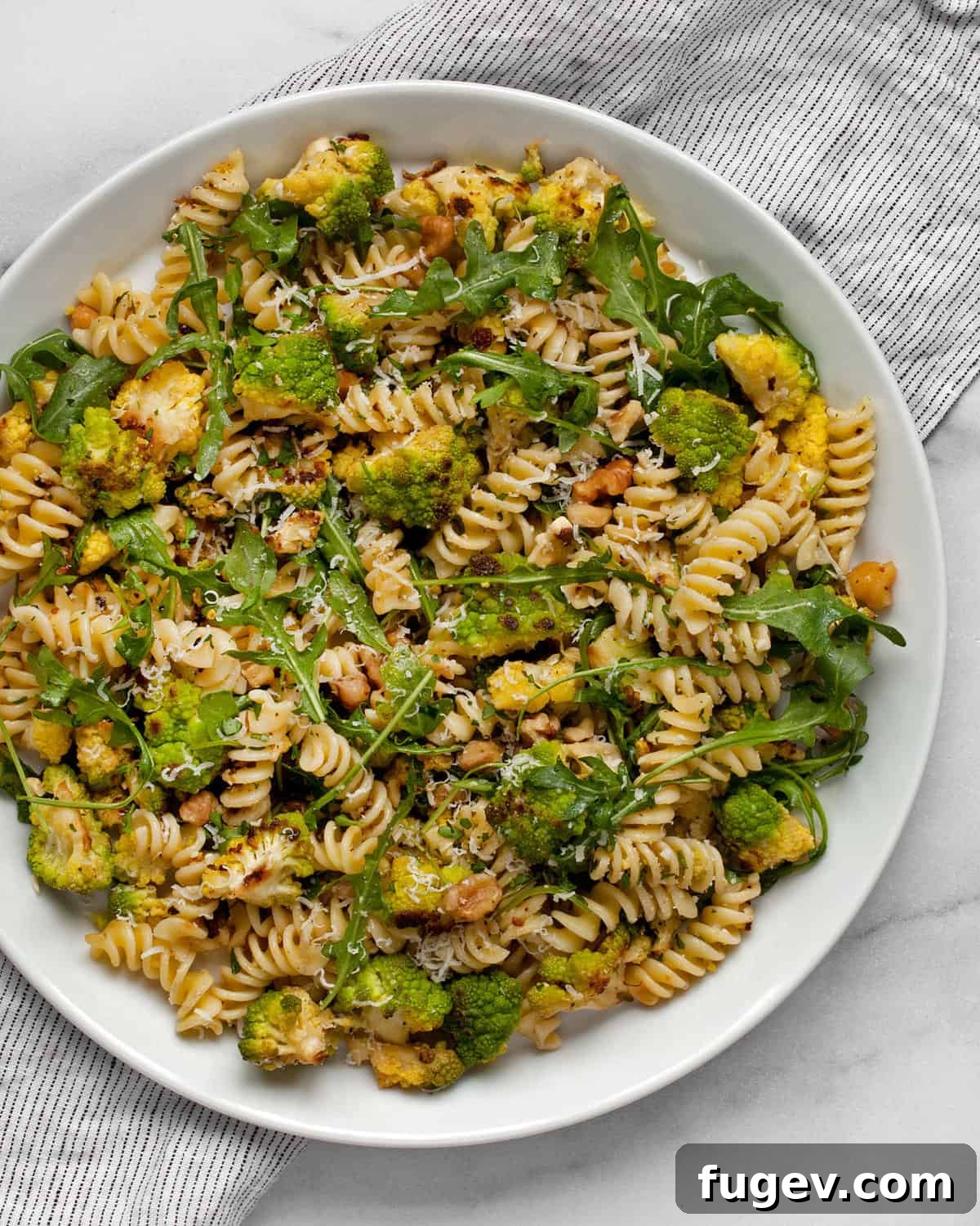 Vibrant Roasted Romanesco Arugula Pasta 2 A close-up of Roasted Romanesco Arugula Pasta on a rustic white plate, garnished with fresh parsley and grated cheese.