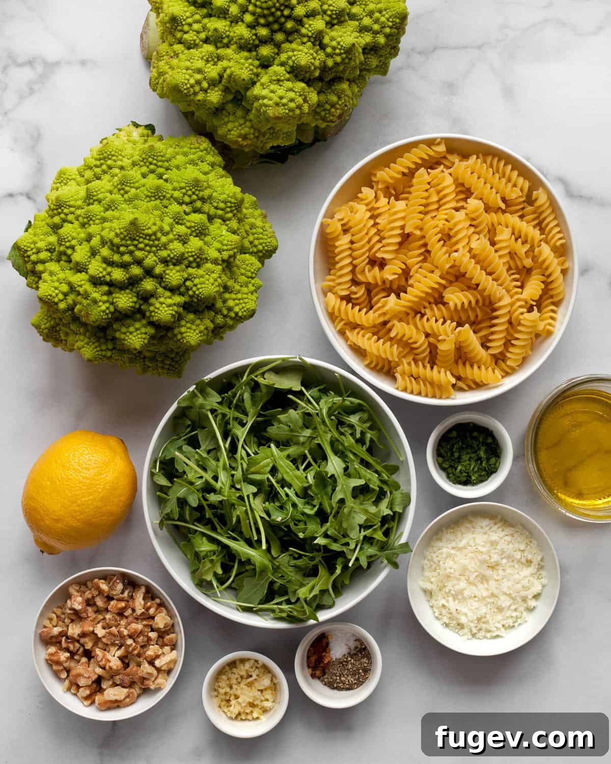 Vibrant Roasted Romanesco Arugula Pasta 3 A collection of fresh ingredients for romanesco pasta, including romanesco heads, dry pasta, fresh arugula, walnuts, Pecorino cheese, garlic, lemon, and a bottle of olive oil.
