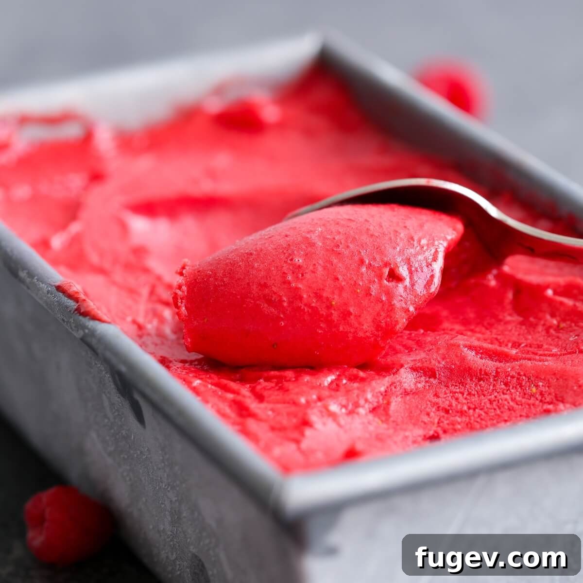 Crimson Berry Bliss 3 Raspberry sorbet being scooped from a metal canister with a silver spoon, showing its smooth texture.