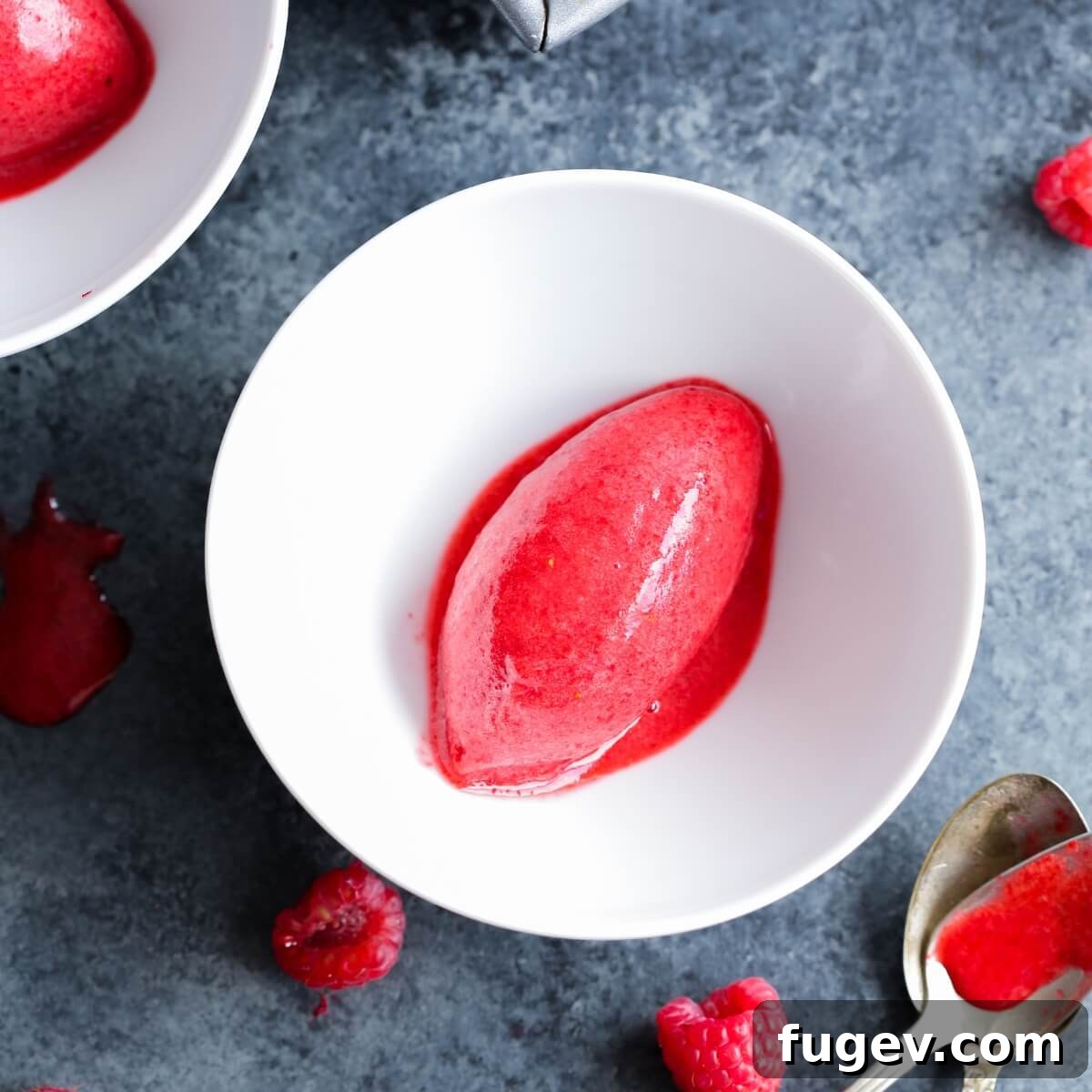 Crimson Berry Bliss 4 A scoop of homemade raspberry sorbet in a white bowl, set against a dark marble background.