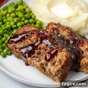 Brown sugar glazed meatloaf on a white plate with sauce drizzled over.