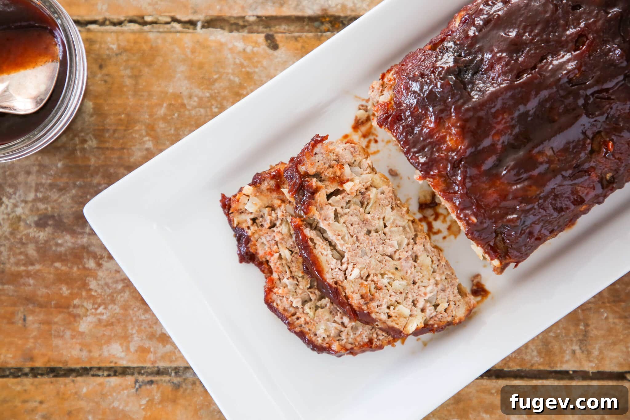 Sticky-Sweet Brown Sugar Meatloaf 9 Two slices of brown sugar glazed meatloaf cut from the main loaf, served on a white plate with fresh rosemary garnish.
