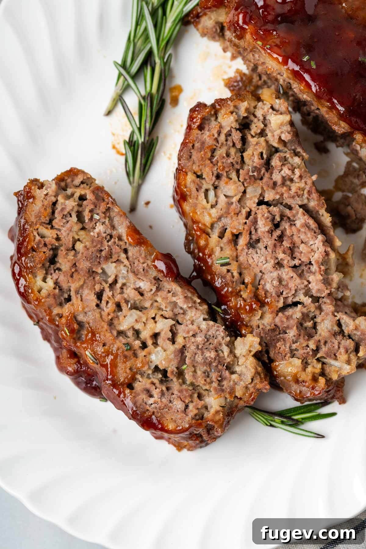 Sticky-Sweet Brown Sugar Meatloaf 10 A slice of brown sugar glazed meatloaf garnished with fresh rosemary on a white plate.