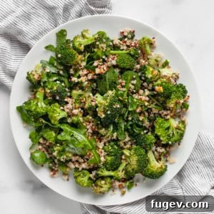 A serving of roasted broccoli quinoa salad on a light grey plate with a fork.