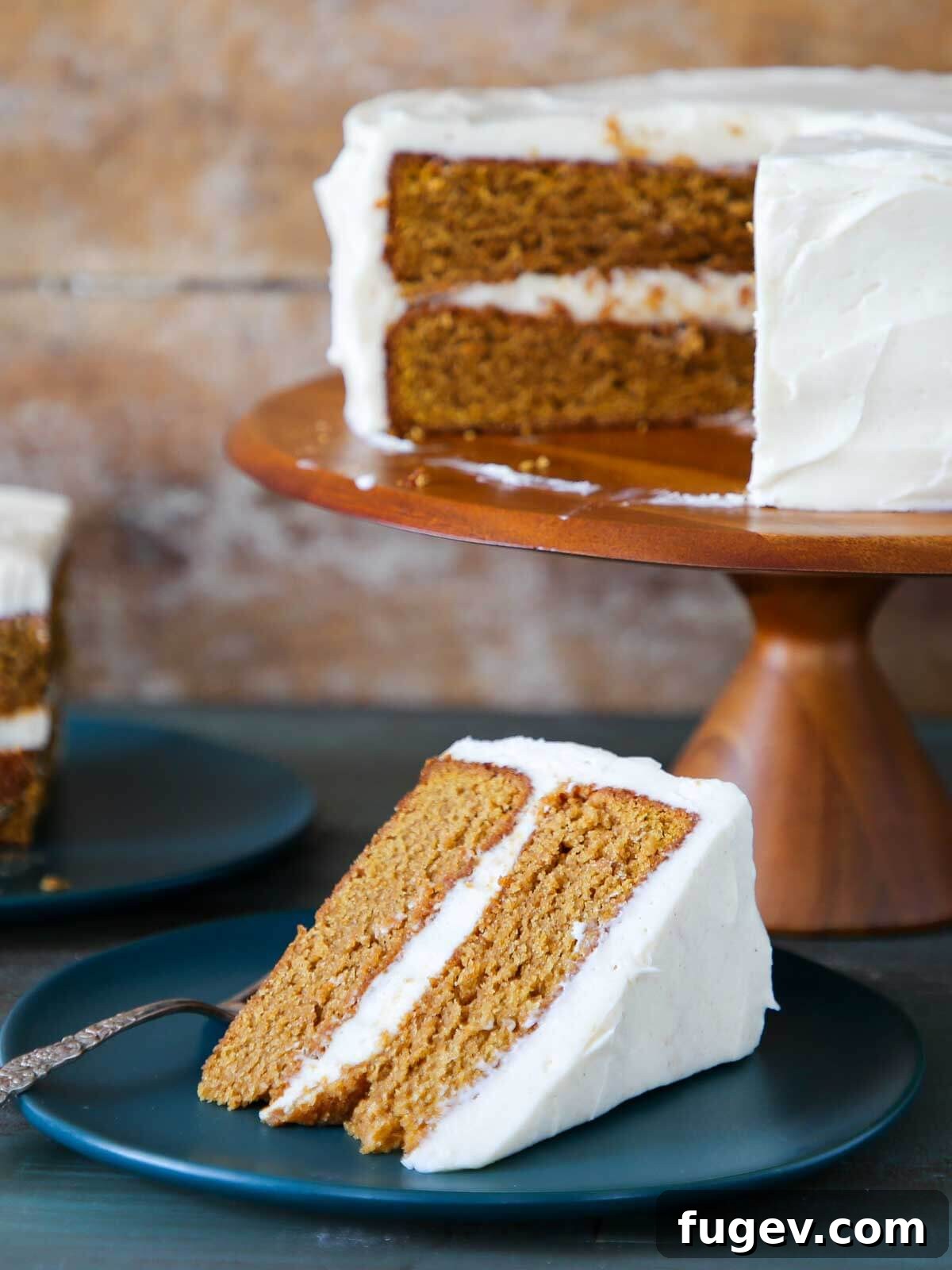 Pumpkin Spice Dream Cake 2 A whole pumpkin cake with a plated slice ready for eating. The cake is covered in a thick layer of white cream cheese frosting.