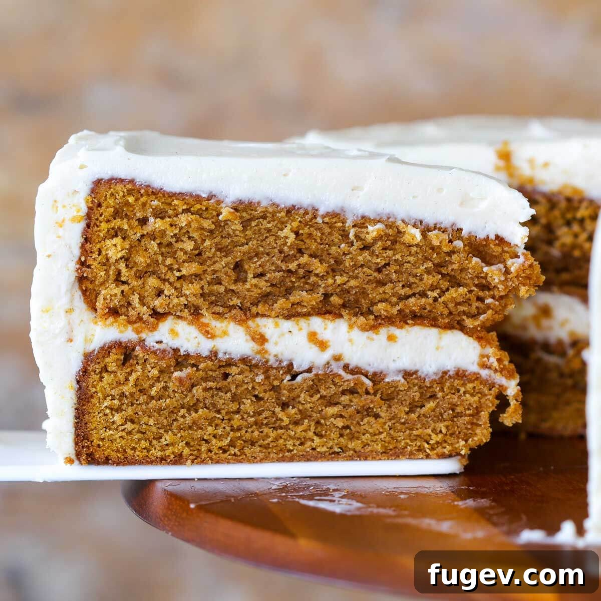 Pumpkin Spice Dream Cake 4 A slice of pumpkin cake being removed from the cake with a white cake server, showing the layers of cake and frosting.