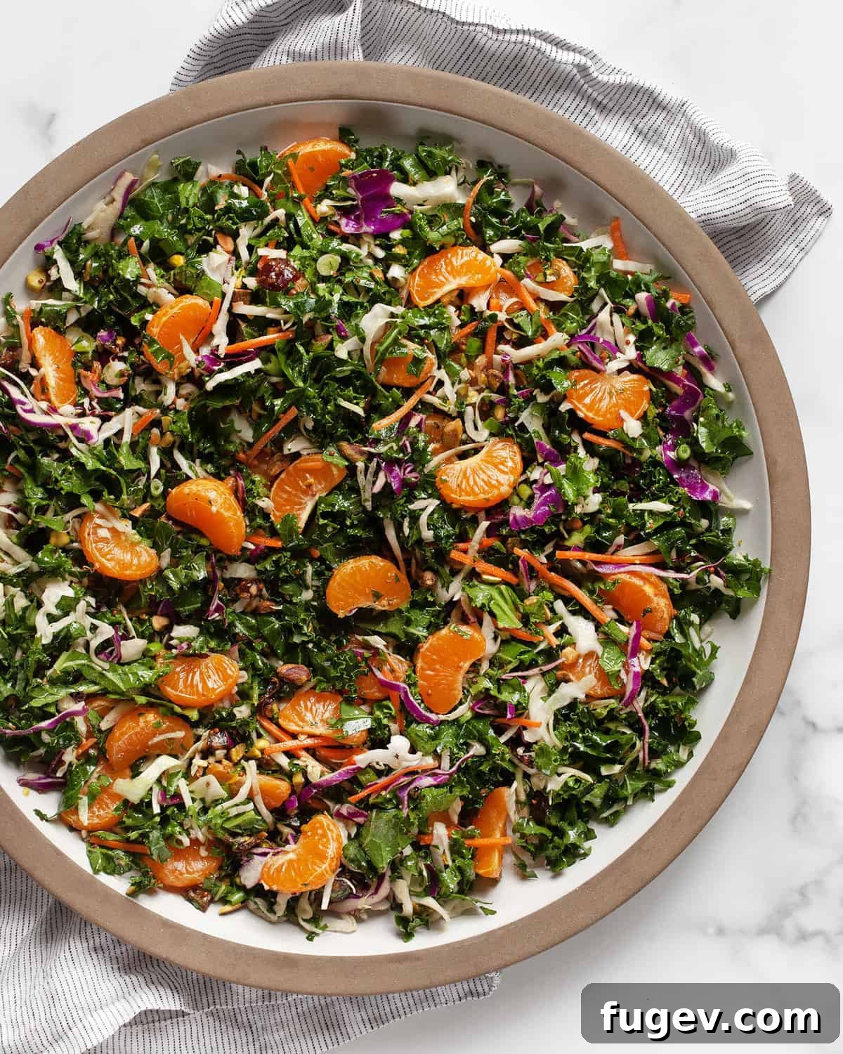 Zesty Mandarin Salad 2 A large, vibrant bowl of Mandarin Orange Salad featuring segments of bright orange mandarins, dark green kale, purple and green cabbage, and chopped pistachios.