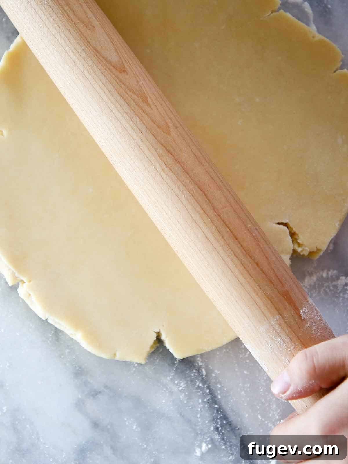 Sweet Tart Dough 2 Pâte Sucrée dough disk being rolled by a wooden pin on a marble surface, ready for baking.