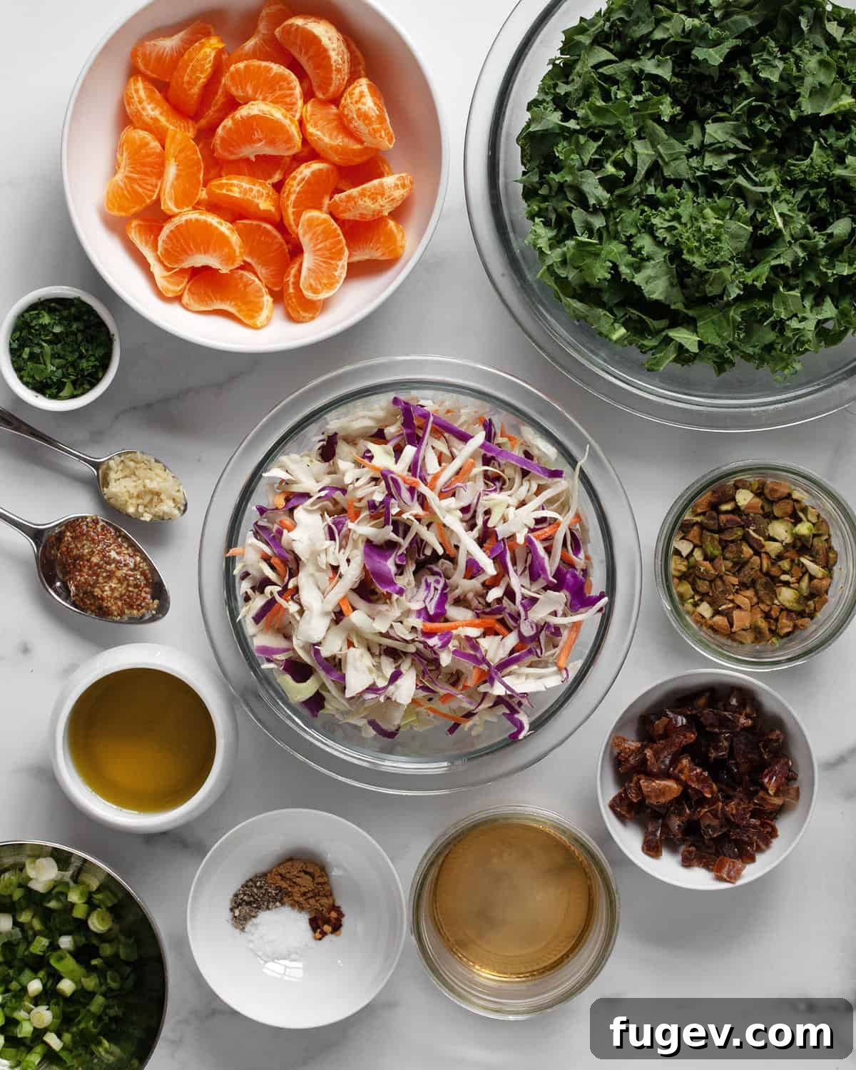 Zesty Mandarin Salad 3 A colorful array of fresh ingredients laid out, including vibrant mandarin oranges, dark green kale, a bag of coleslaw mix, pistachios, scallions, dates, and small bowls with spices, garlic, olive oil, and white wine vinegar.