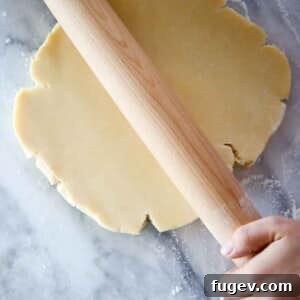 Sweet Tart Dough 8 pate sucree dough disk being rolled by wooden pin on marble.