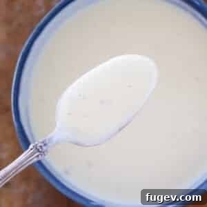 Elegant Vanilla Custard Drizzle 6 creme anglaise on spoon over bowl.