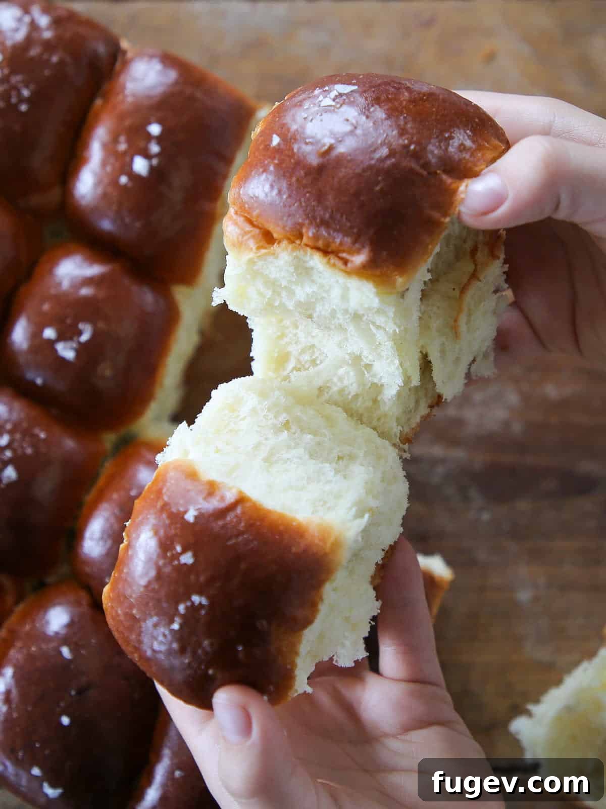 Pillowy Potato Rolls 2 Breaking a warm, fluffy potato roll by hand to reveal its tender, steamy interior, showcasing the soft texture.
