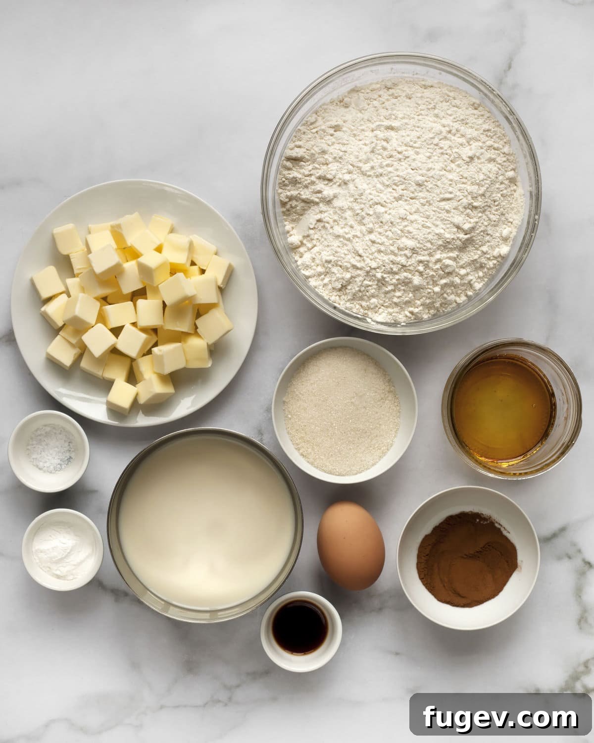 Cozy Cinnamon Scones 3 Various ingredients for scones including flour, butter, sugar, cinnamon, baking powder, egg, vanilla extract and salt laid out on a surface.