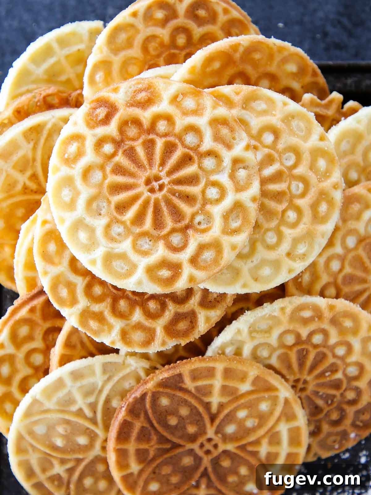 Sweet Italian Iron-Pressed Delights 2 Pizzelle cookies piled high on a black tray, dusted with powdered sugar.