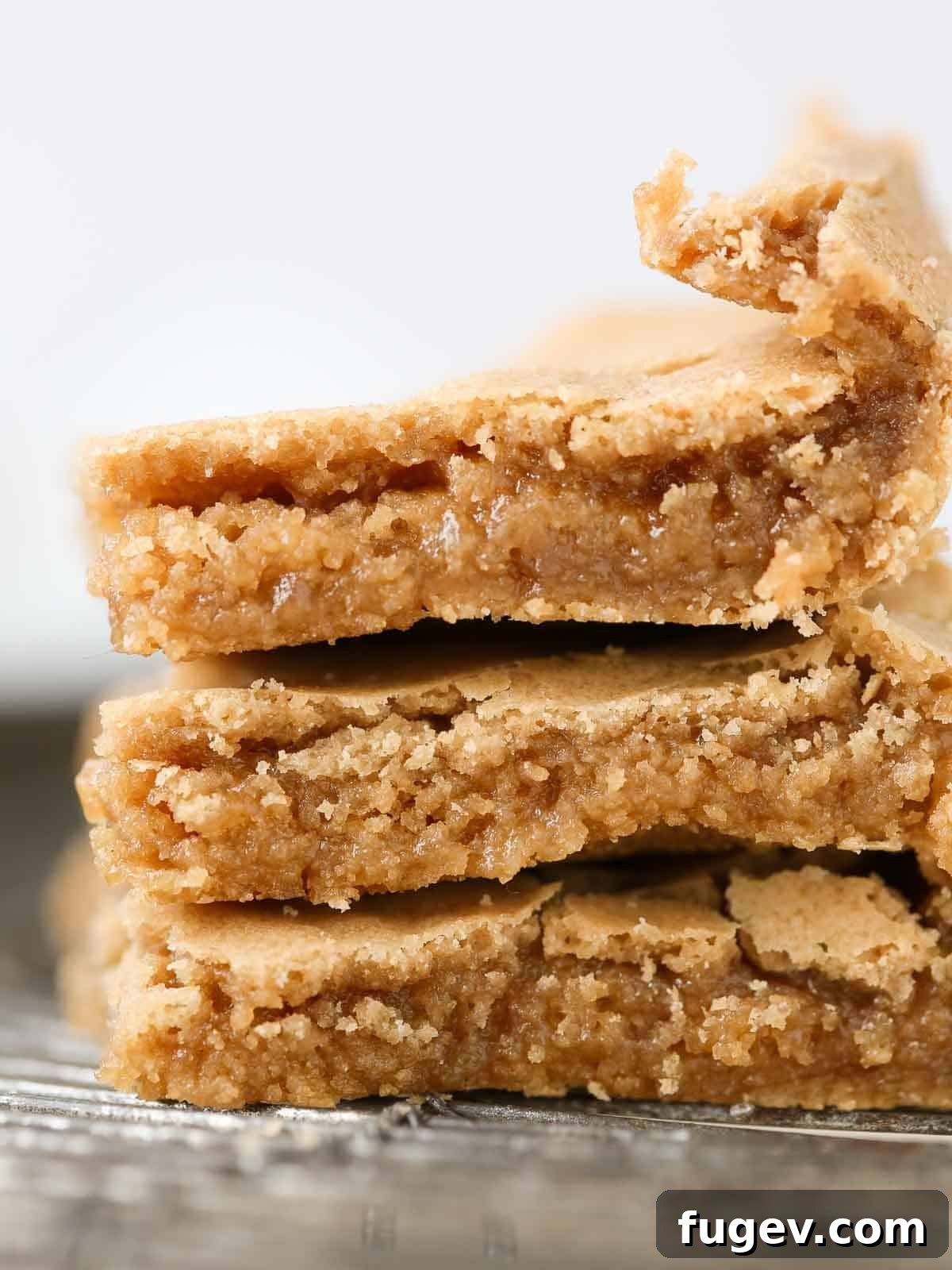 Butterscotch Blondies 5 Three butterscotch brownies stacked neatly on a wire cooling rack, showcasing their thick, chewy centers and golden edges.