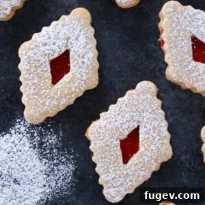 20 Festive Christmas Cookie Recipes 29 Raspberry Linzer Cookies on dark surface with extra powdered sugar.