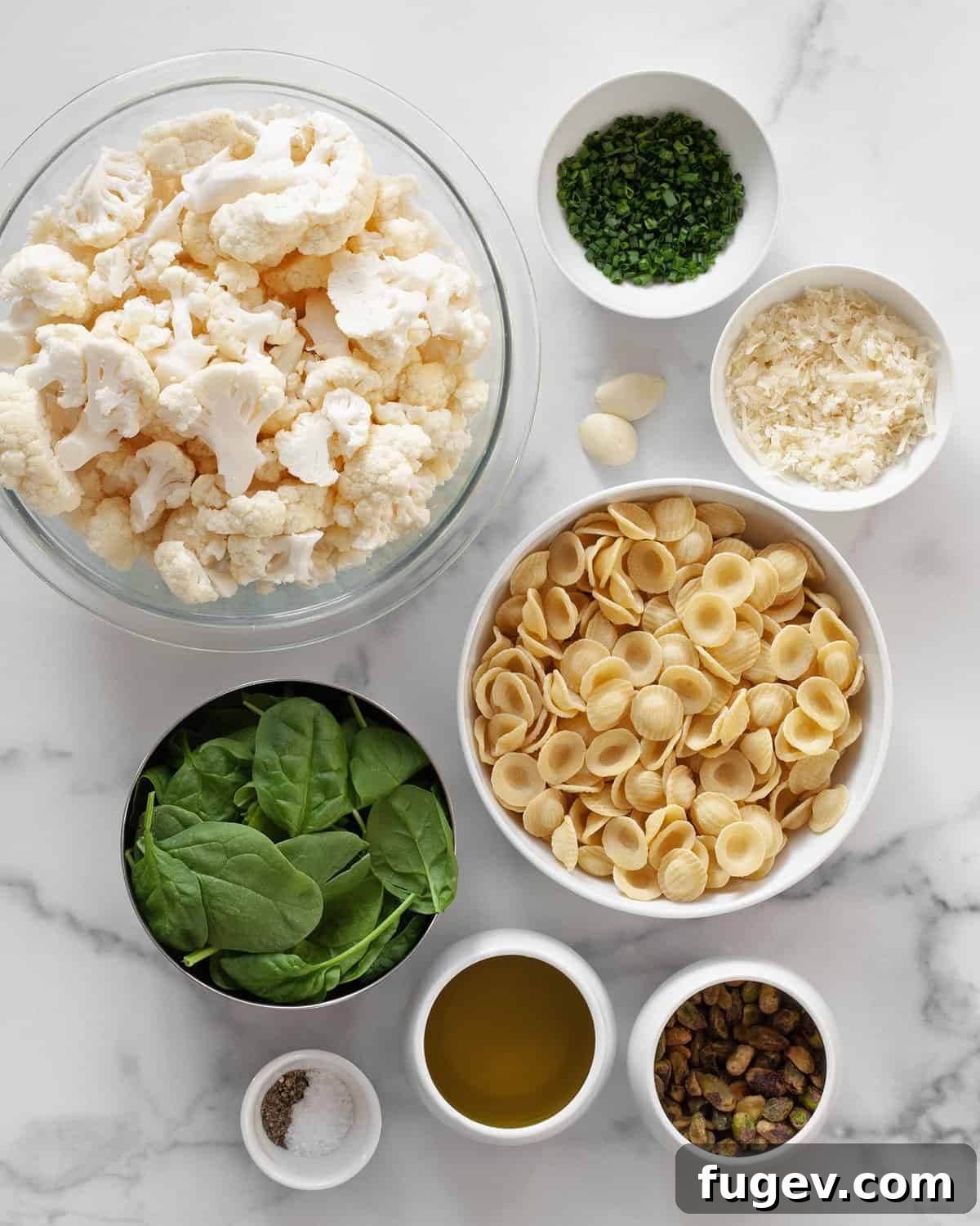 Golden Roasted Cauliflower Pasta with Spinach Pesto 3 A flat lay photograph showcasing all the fresh ingredients for roasted cauliflower pasta: cauliflower, spinach, Parmesan, pistachios, olive oil, garlic, chives, salt, and pepper.