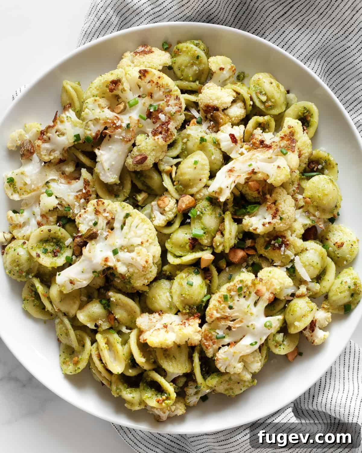 Golden Roasted Cauliflower Pasta with Spinach Pesto 7 A close-up of roasted cauliflower pasta with spinach pesto on a white plate, garnished with fresh herbs.