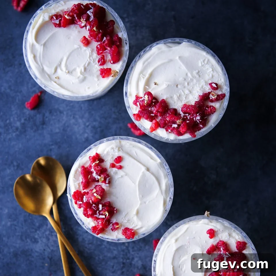 Velvet Raspberry White Chocolate Dream 7 White Chocolate Raspberry Mousse served in a clear glass, with a spoon ready to enjoy, highlighting its smooth texture.