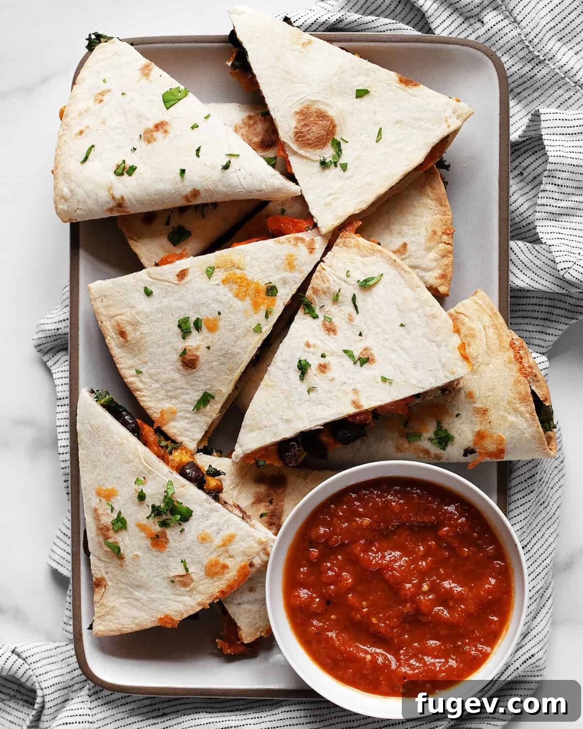 Savory Roasted Sweet Potato Black Bean Quesadillas 2 Golden brown roasted sweet potato black bean quesadillas cut into wedges on a rustic white plate, garnished with fresh cilantro.
