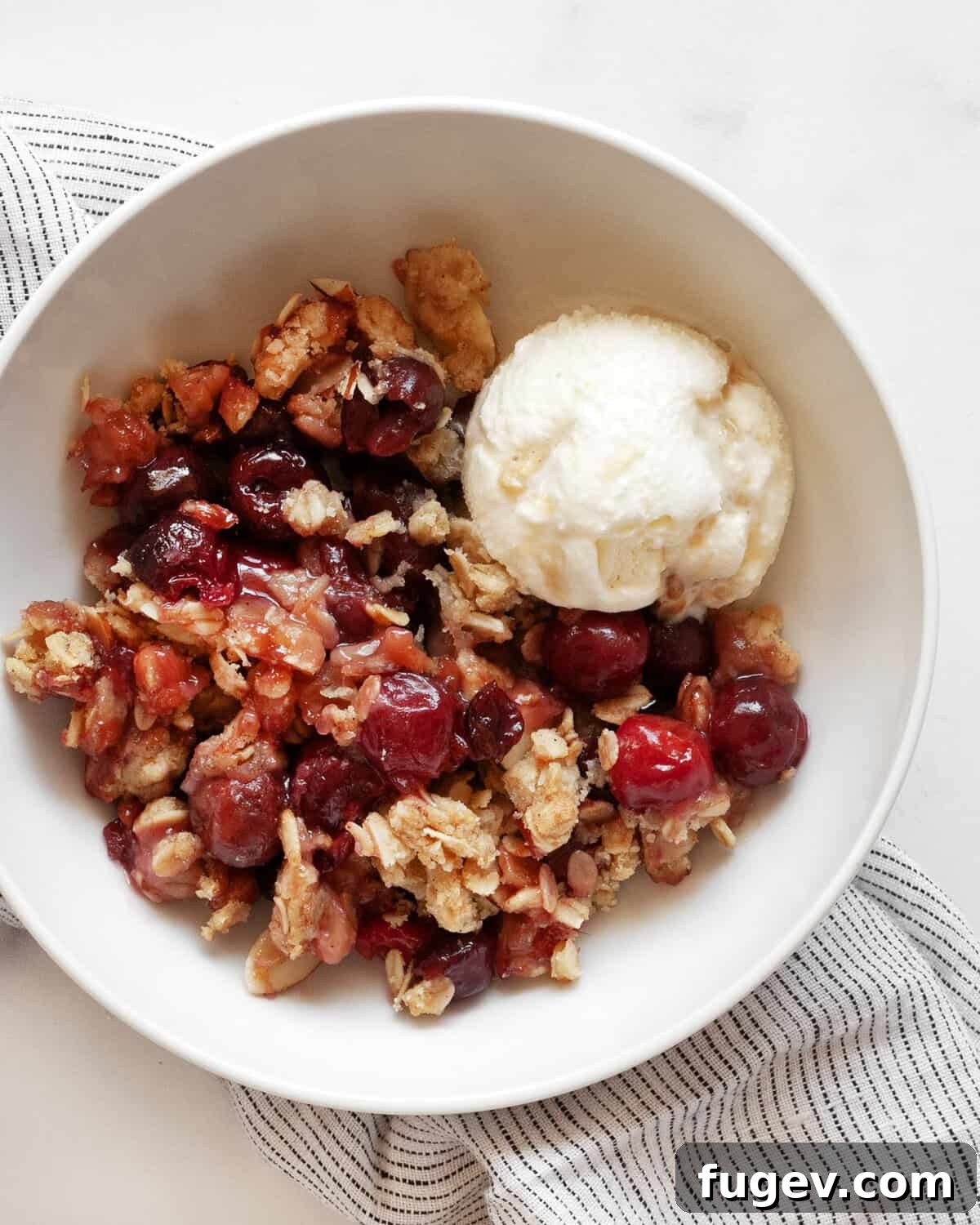 Quick Delicious Cherry Crumble 7 A small bowl holding a warm serving of cherry crumble, beautifully topped with a scoop of melting vanilla ice cream.