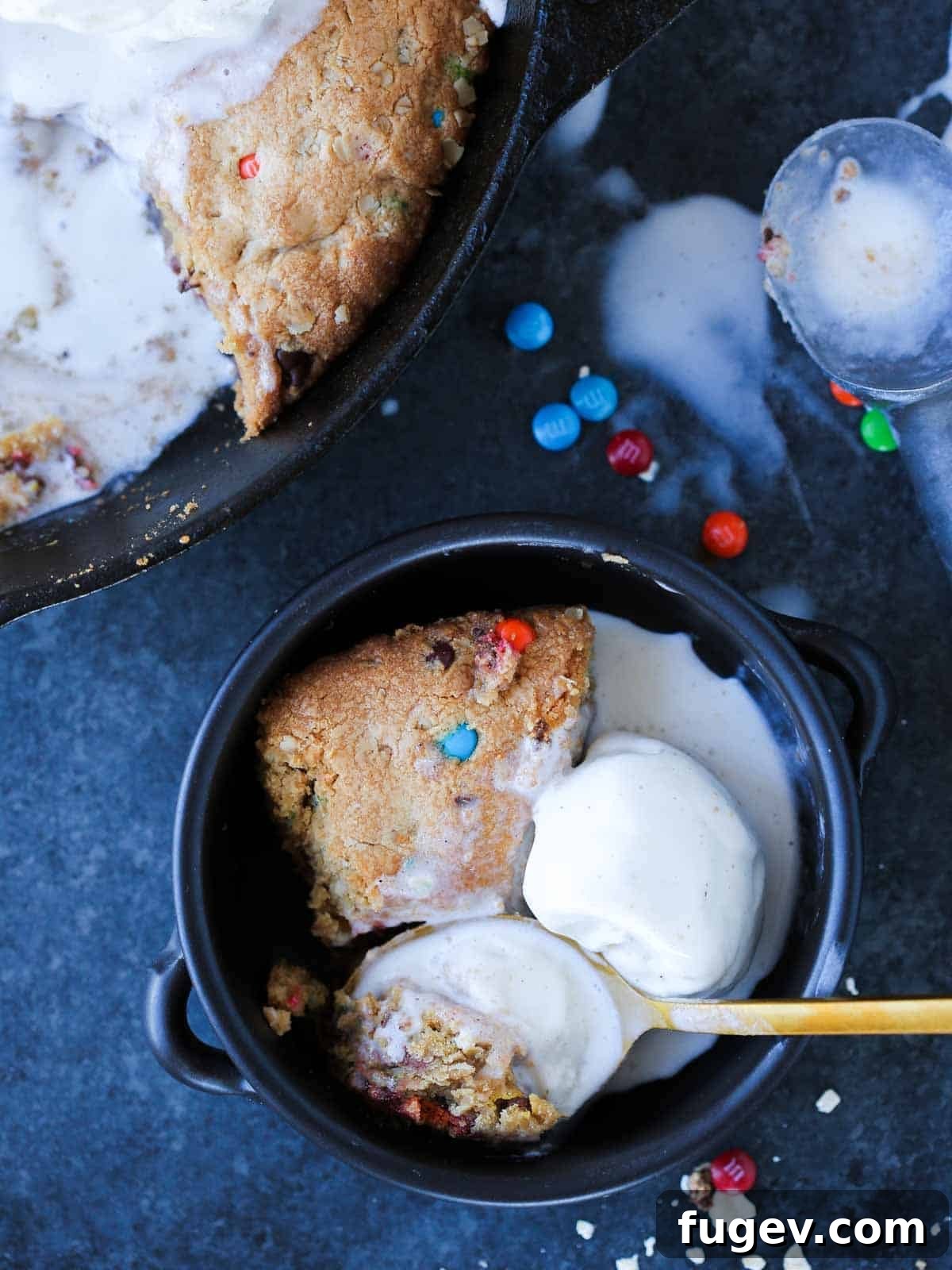 Deep Dish Cookie 3 Pizookie served on a black surface with a separate bowl of ice cream, showing its perfectly baked edges.