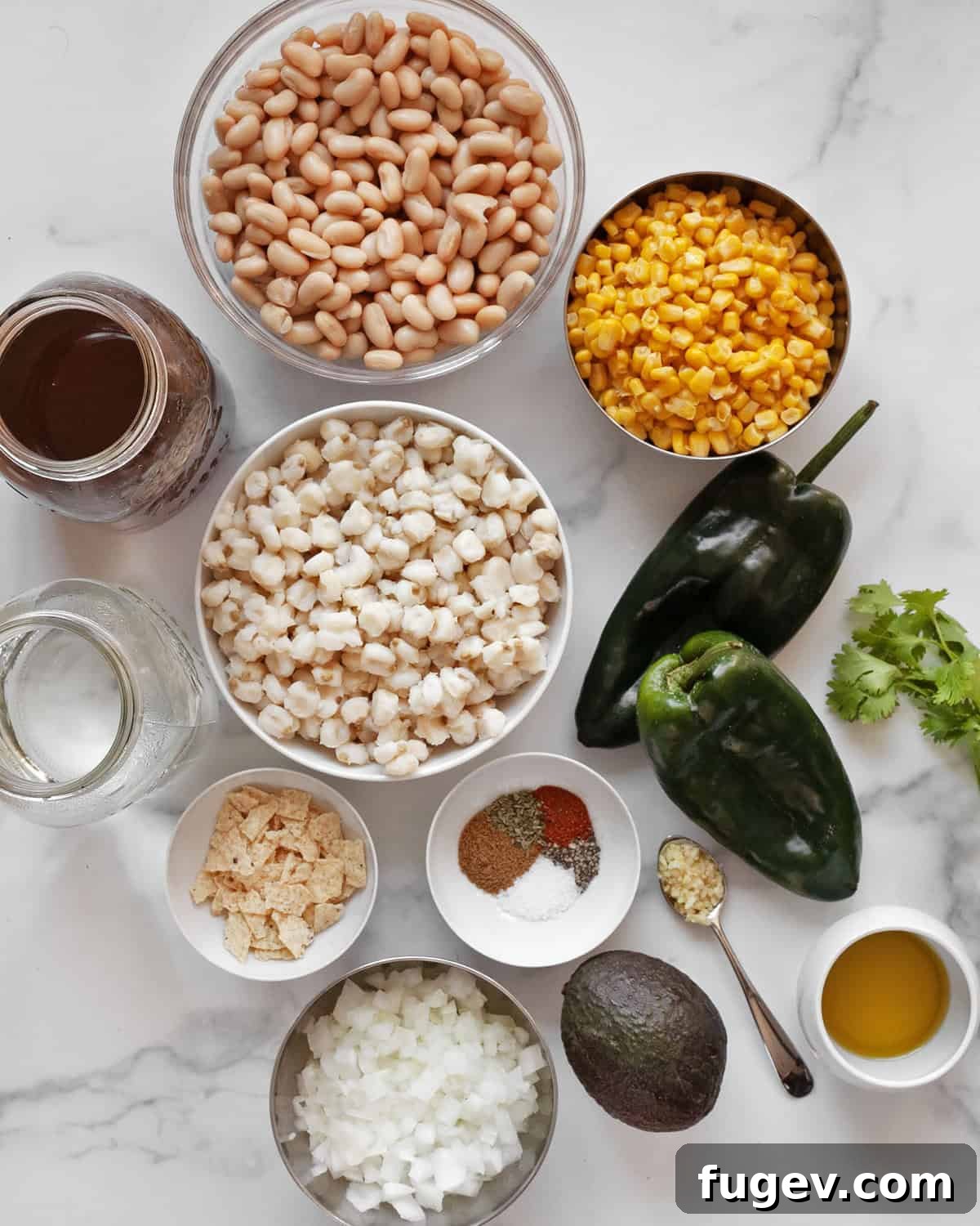 Creamy Vegan Poblano White Bean Chili 3 A vibrant selection of ingredients for vegan white bean chili, including cannellini beans, fresh corn, hominy, green poblano peppers, onion, garlic, assorted spices, vegetable broth, cilantro, ripe avocado, and tortilla chips.