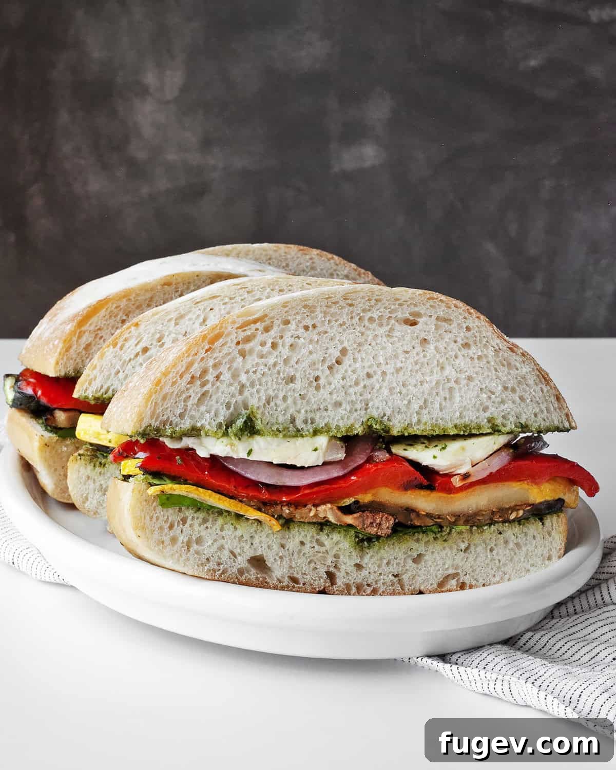 Mediterranean Grilled Vegetable Ciabatta 7 Two freshly prepared ciabatta sandwiches with grilled vegetables, pesto, and mozzarella, cut in half and served on a plate.