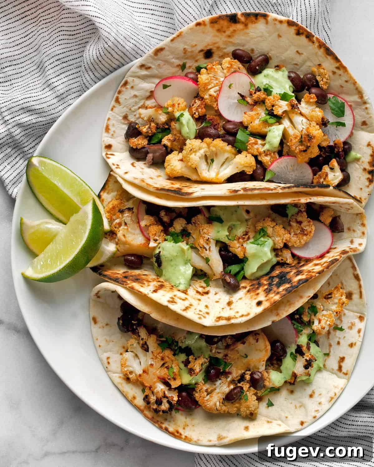 Smoky Chipotle Cauliflower Tacos 2 Three roasted cauliflower tacos artfully arranged on a plate, garnished with fresh lime slices and cilantro.
