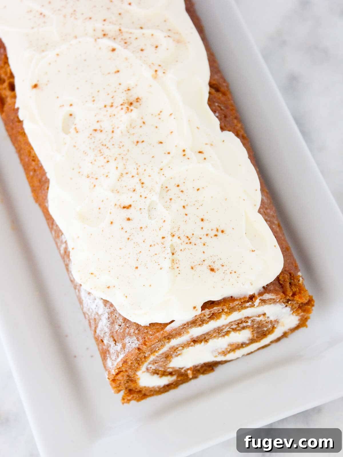 Spiced Pumpkin Roll Perfection 3 Unsliced pumpkin roll with a dusting of cream cheese frosting on top.