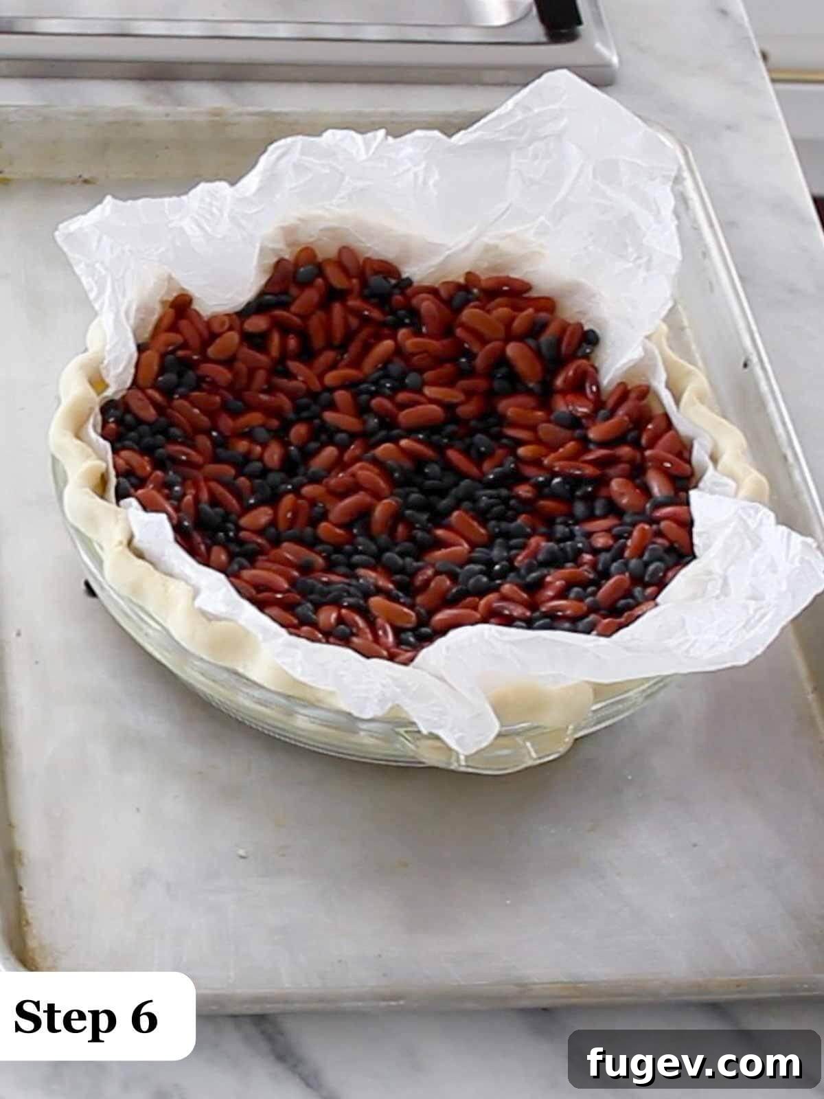 Decadent Chocolate Pecan Pie 7 Text: Step 6, a pie crust in a tin filled with dried beans acting as pie weights during par-baking.