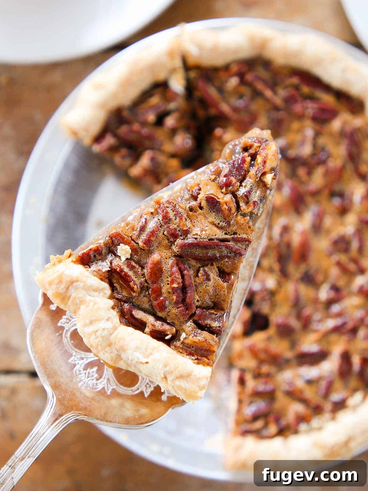 The Perfect Pecan Pie 2 A perfectly sliced pecan pie on a pie server, showcasing its rich, golden-brown filling and whole pecans, with the rest of the pie in the background.