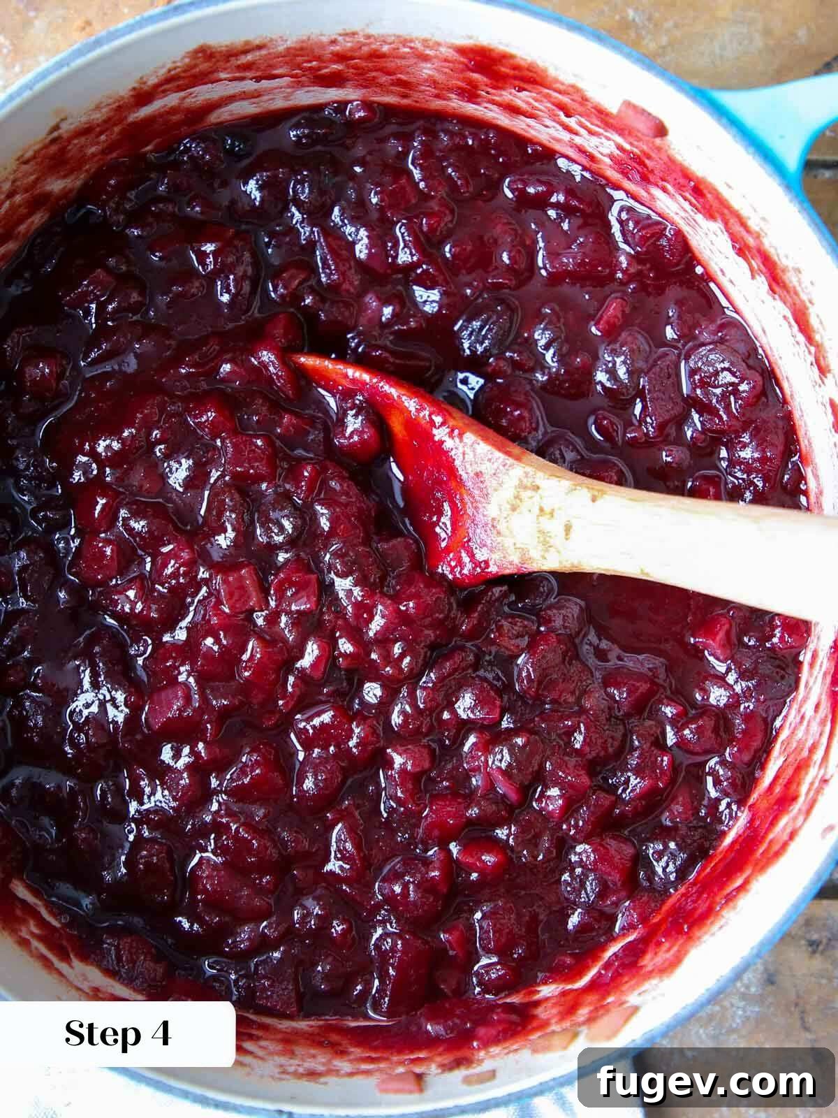 Ruby Red Cranberry Chutney 5 Cooked cranberry chutney simmering in a pot with a wooden spoon, showing its thickened texture and rich color.