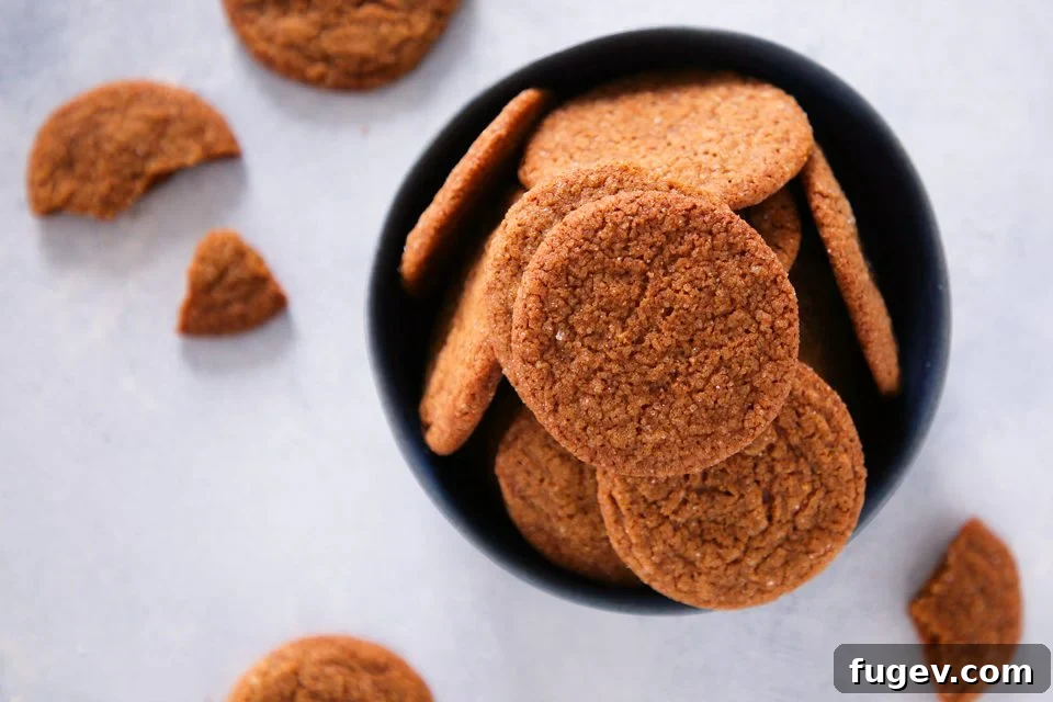 Timeless Gingersnap Cookies 4 A stack of gingersnap cookies on a wooden board, highlighting their inviting golden color and cracked tops.