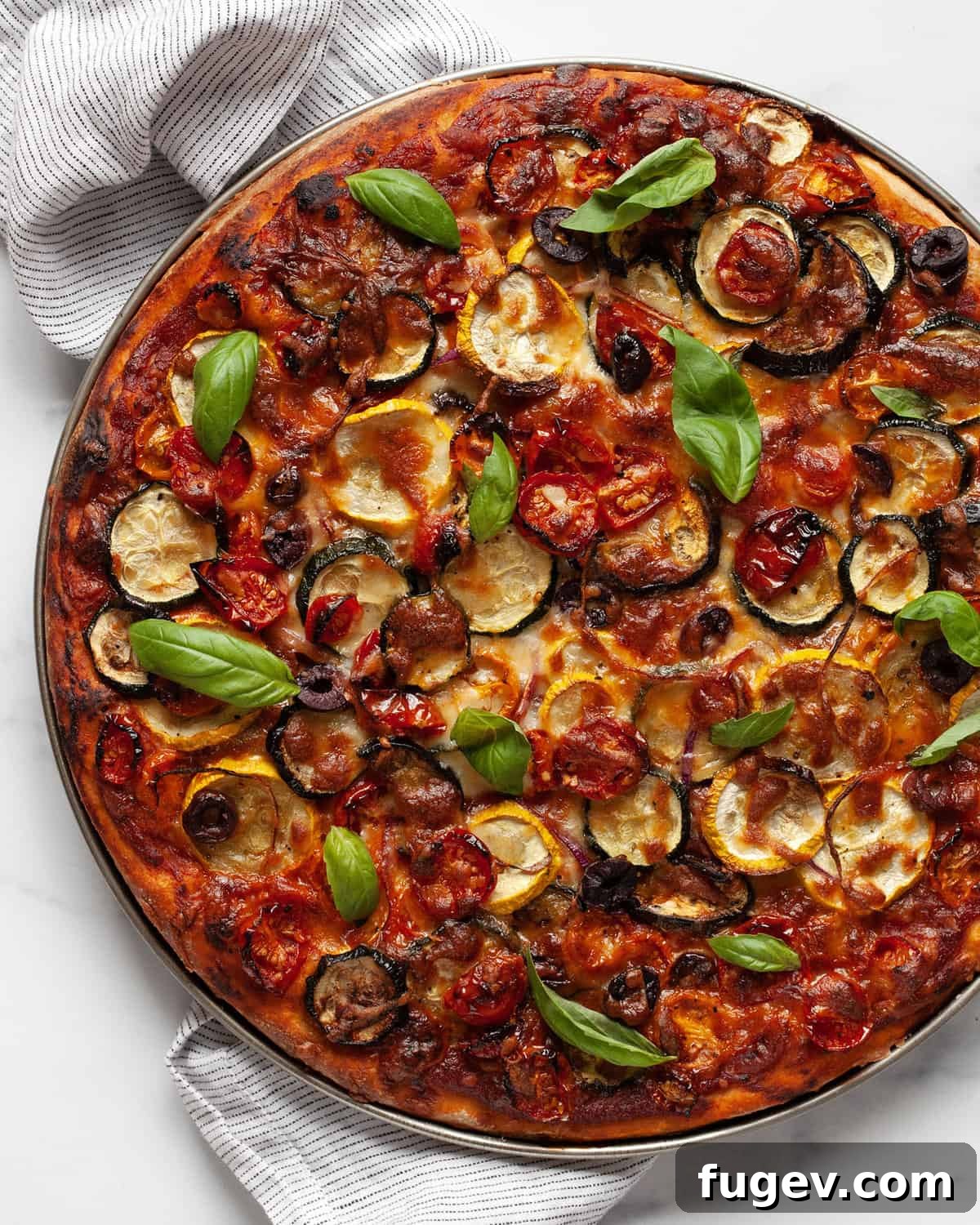 Garden Roast Pizza 2 A beautifully baked roasted vegetable pizza, generously topped with fresh basil leaves, ready to be sliced.