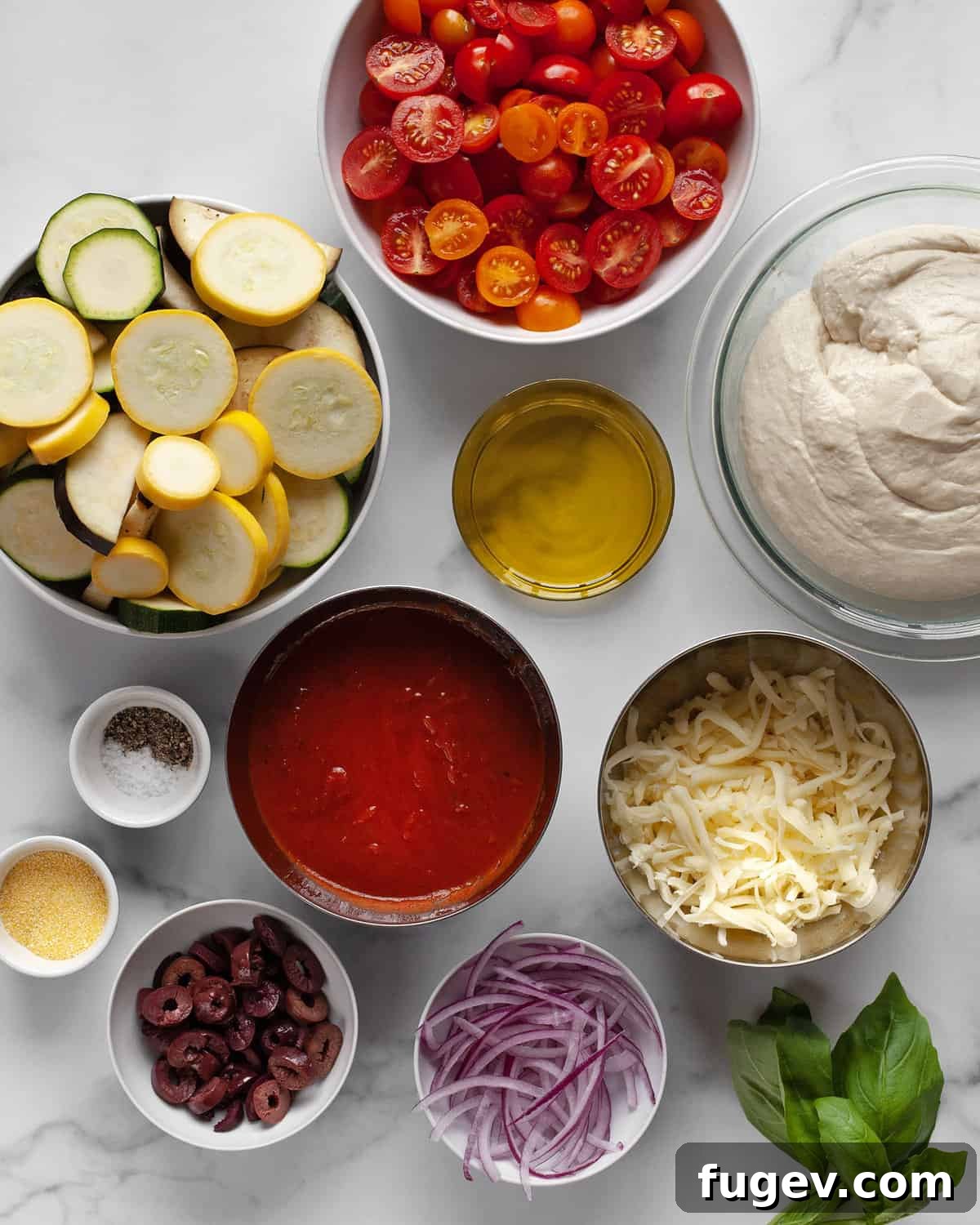 Garden Roast Pizza 3 A flat lay image displaying all the fresh ingredients needed for roasted vegetable pizza, including pizza dough, various sliced vegetables, tomato sauce, shredded mozzarella, olives, red onion, and a bunch of fresh basil.