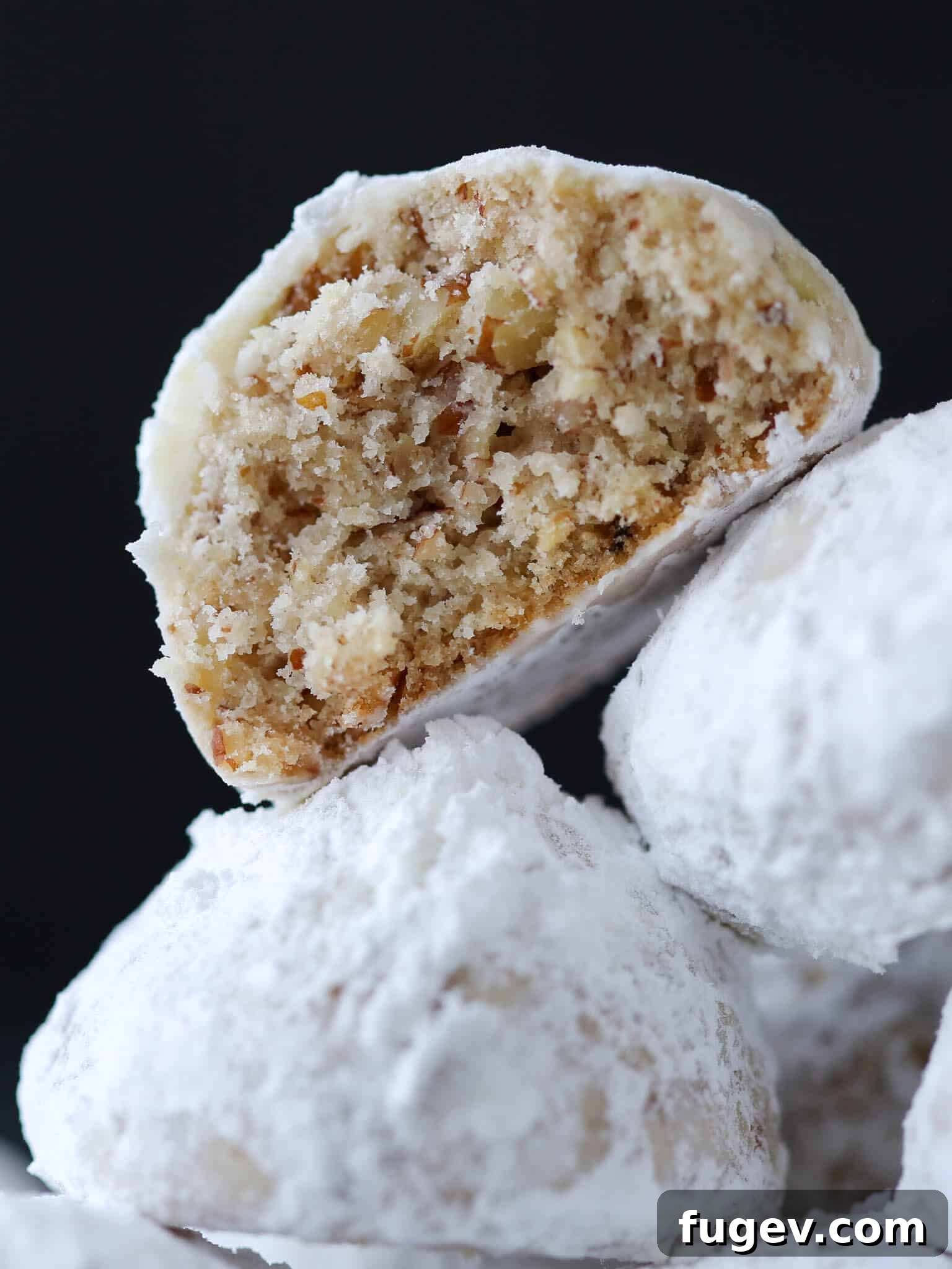 Melt-in-Your-Mouth Snowball Cookies 2 Three snowball cookies with the top one showing a crumbly interior, dusted with powdered sugar.