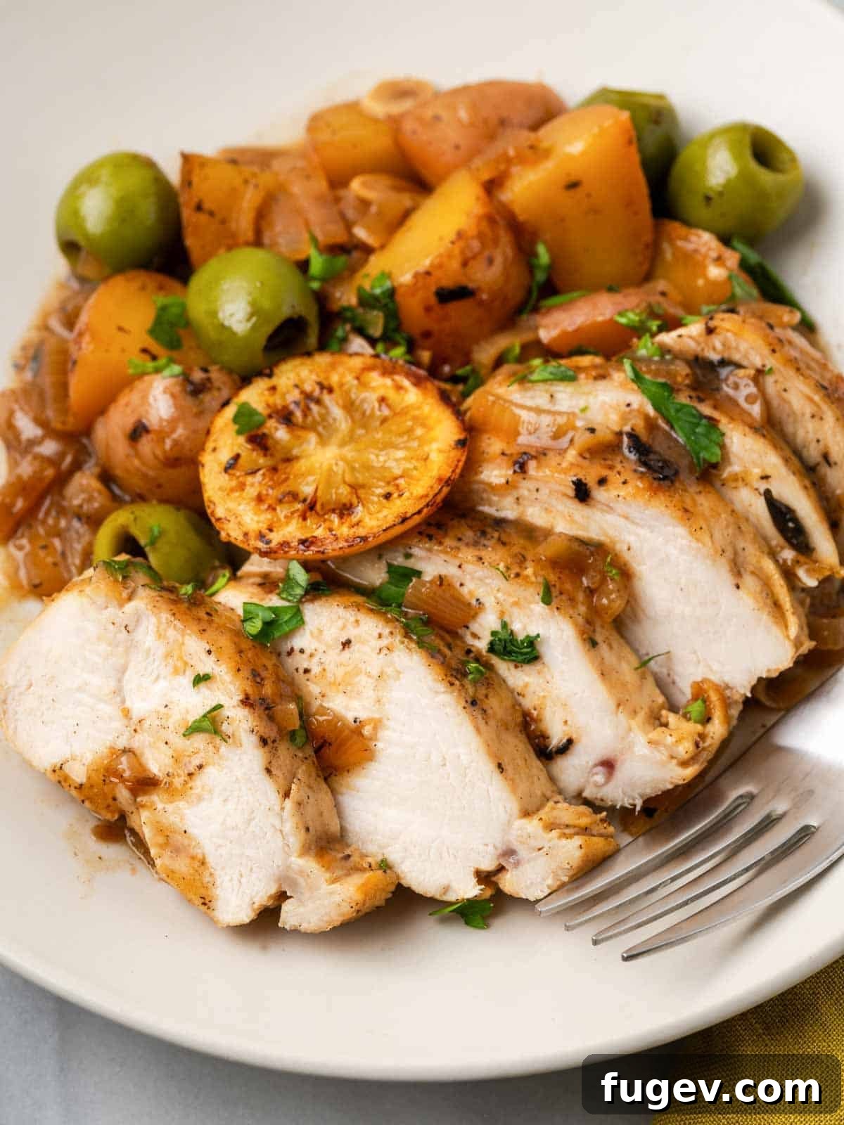 Zesty Lemon Chicken 3 Perfectly sliced lemon chicken on a plate, surrounded by tender roasted potatoes, olives, and garnished with fresh herbs, ready for serving.