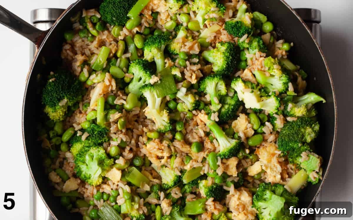 Nutrient-Packed Broccoli, Edamame, and Pea Fried Rice 6 Close-up of broccoli, peas, and edamame stirred into brown rice in a large skillet, ready to serve.