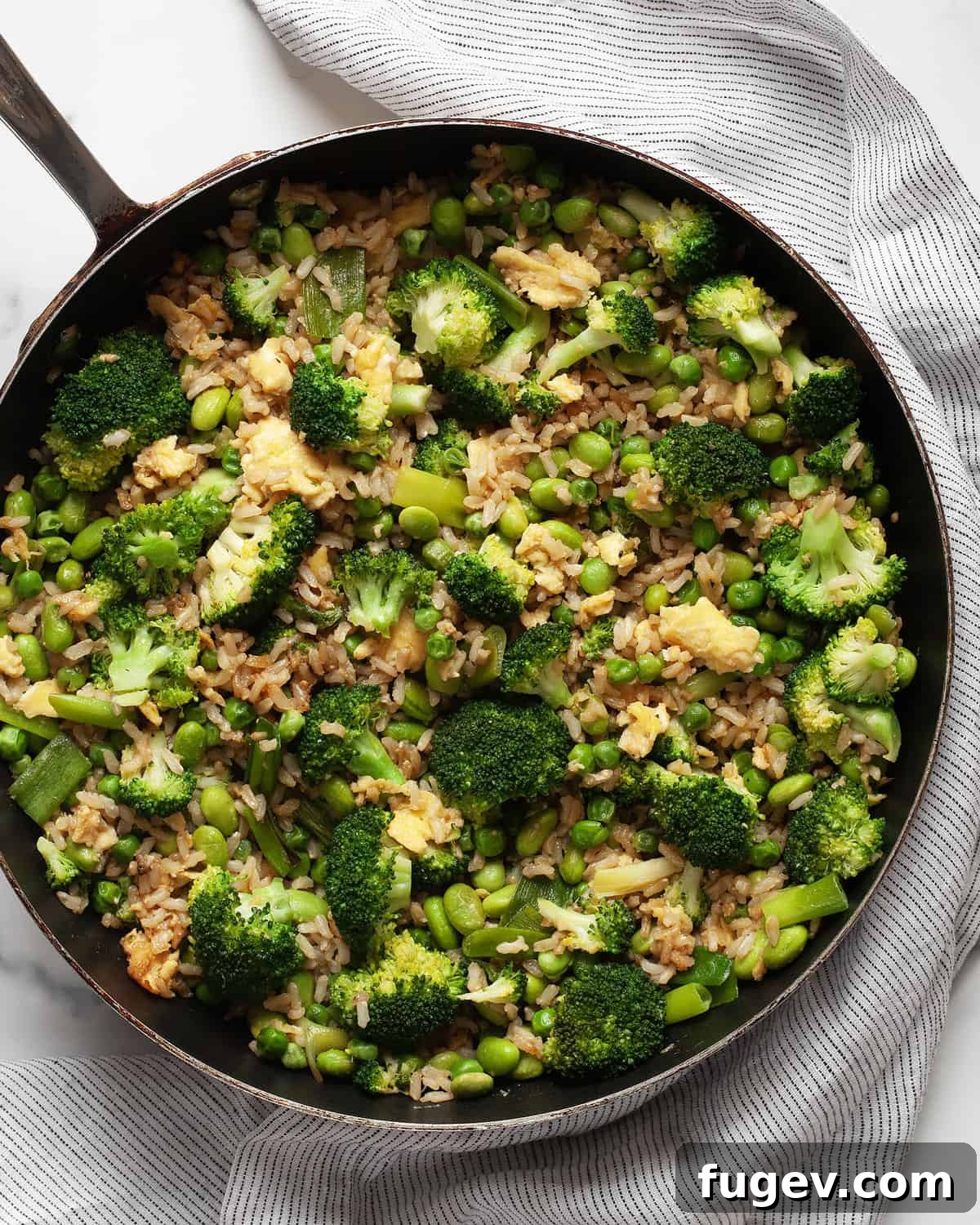 Nutrient-Packed Broccoli, Edamame, and Pea Fried Rice 7 Broccoli, pea and edamame fried rice simmering in a large skillet, ready to be served.