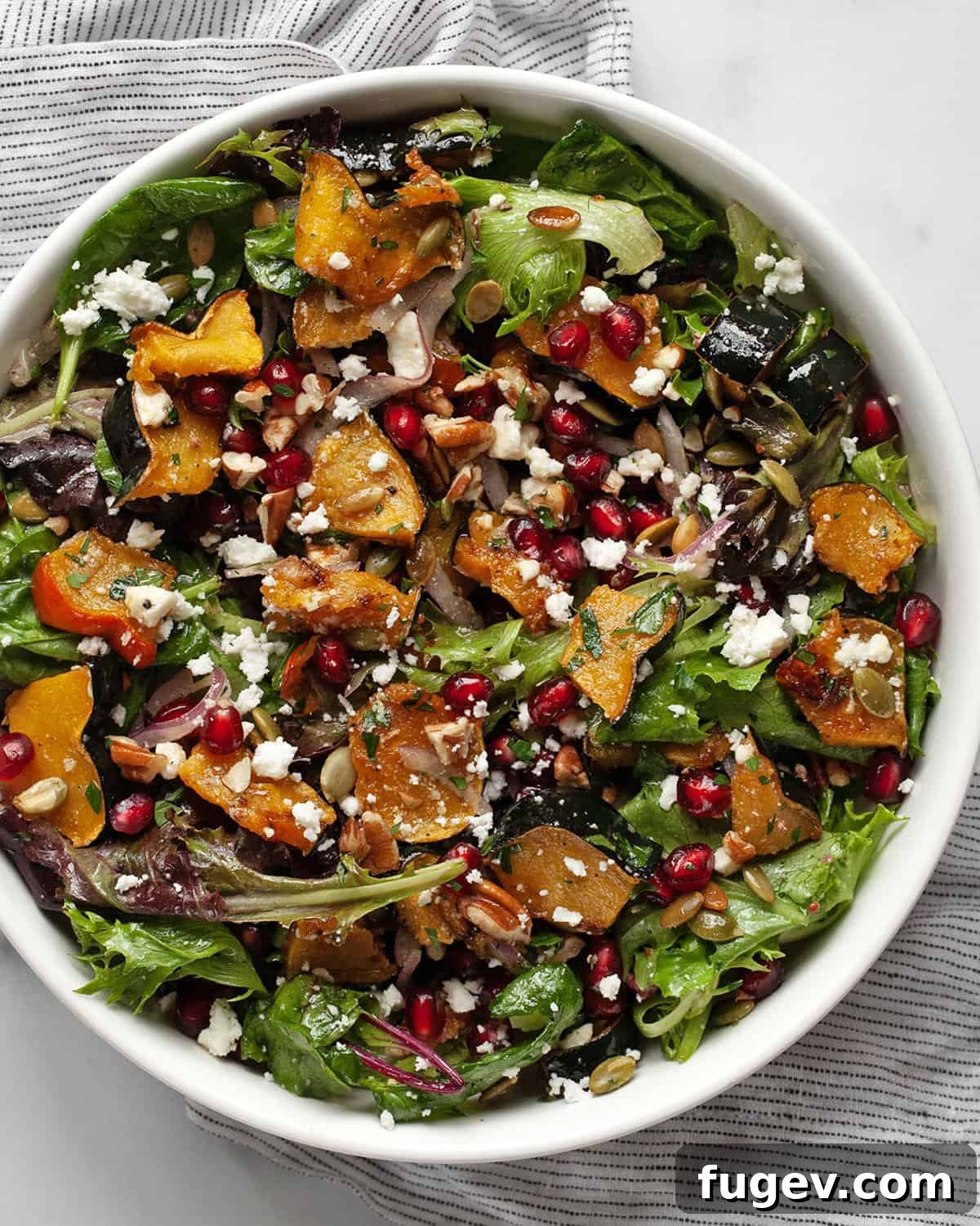 Golden Harvest Squash Salad 7 A close-up of a beautifully composed fall salad in a bowl, featuring roasted acorn squash, glistening pomegranate seeds, crunchy pumpkin seeds, creamy goat cheese, and toasted pecans.