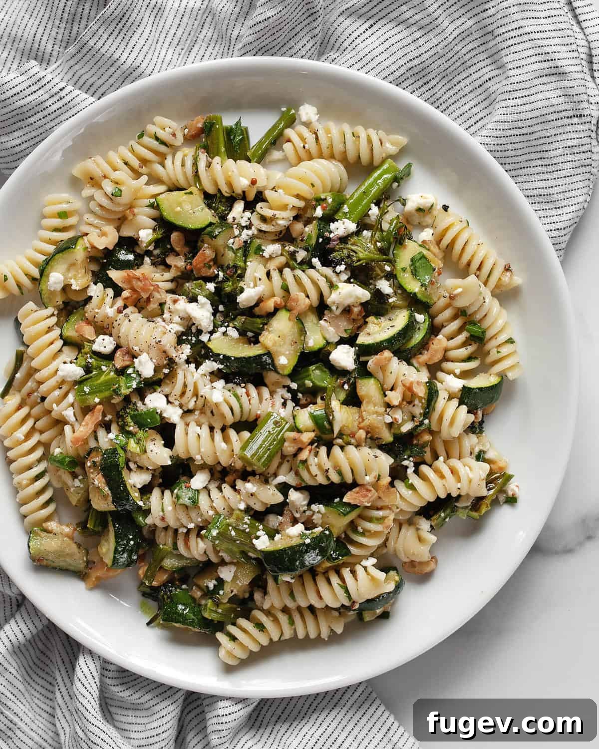 Rustic Roasted Broccolini Zucchini Pasta Salad 2 A beautifully presented pasta salad featuring roasted broccolini and zucchini, artfully arranged on a white plate and garnished with fresh herbs and crumbled feta cheese.
